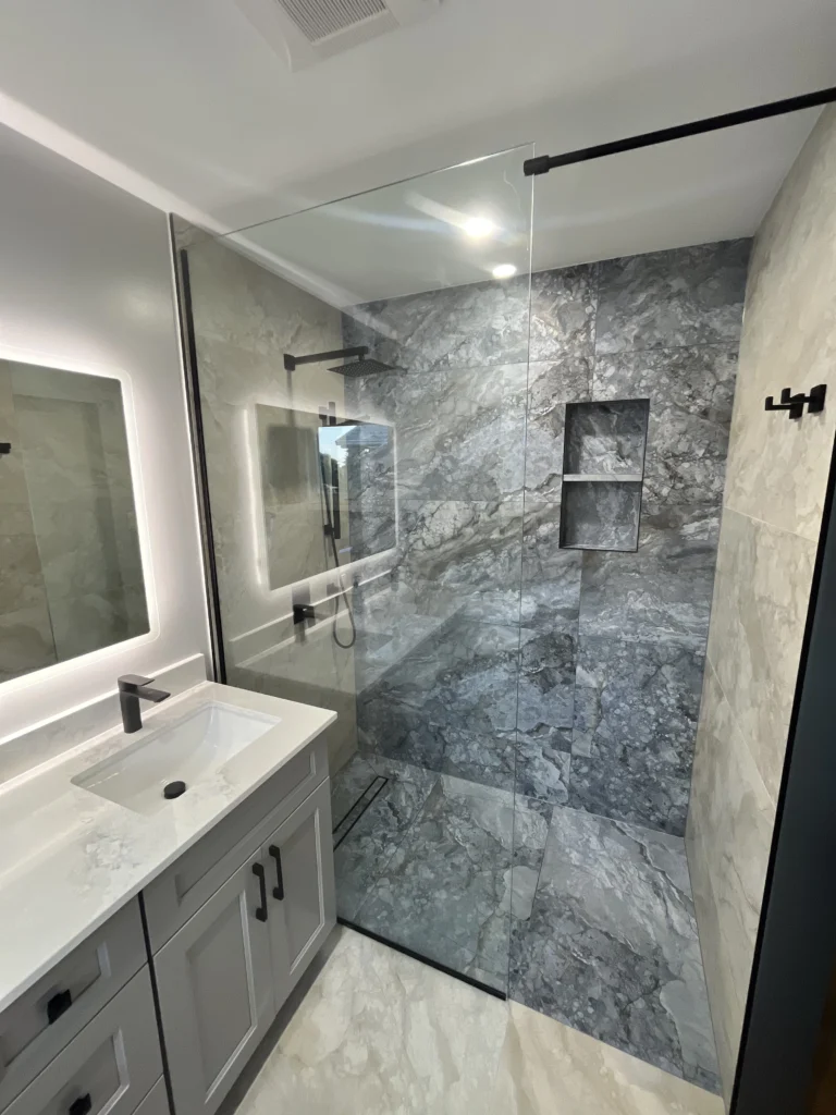 Overhead view of frameless glass shower enclosure with grey marble tiles and matte black hardware