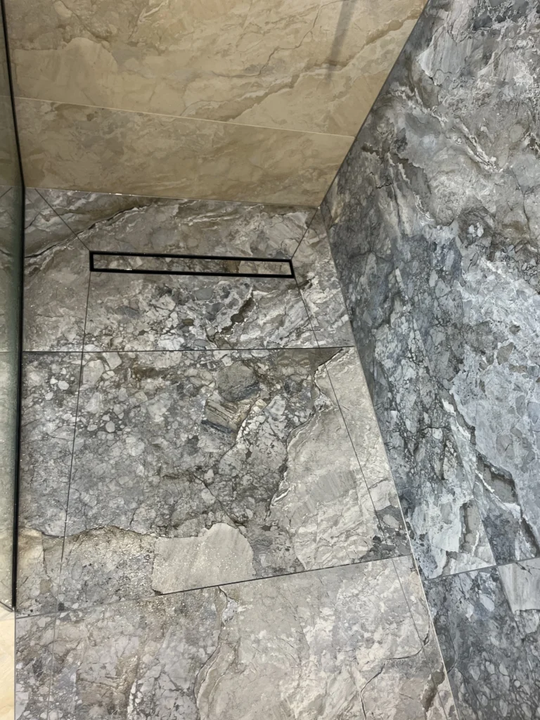 Tile insert linear drain in a shower with blue and grey marble effect tiles