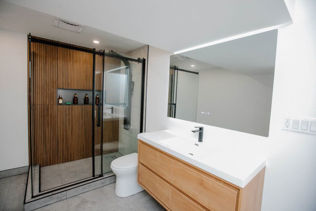Wide shot of the bathroom layout showing the black framed sliding shower door, floating vanity, and gray concrete look floor tiles