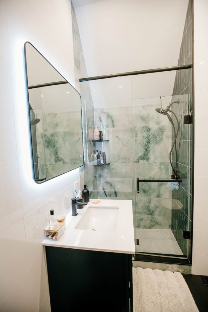 30 inch dark green vanity with white countertop and black faucet next to a green onyx tiled glass shower