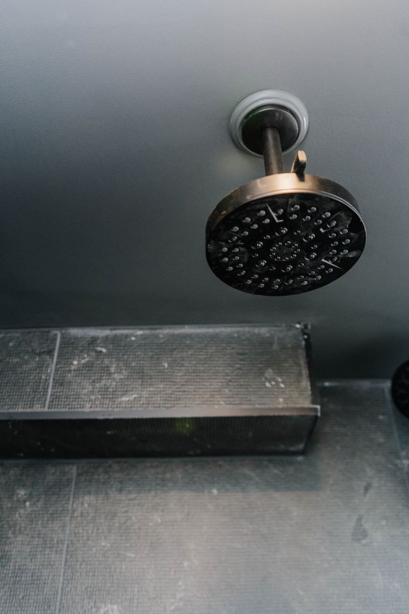 Ceiling mounted matte black rain shower head installed against dark grey slate look porcelain tiles Vaughan