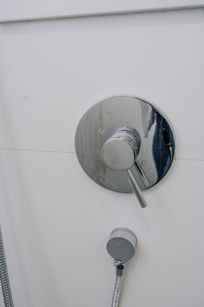 Close up of a modern chrome pressure balance shower valve mounted on large format white wall tiles