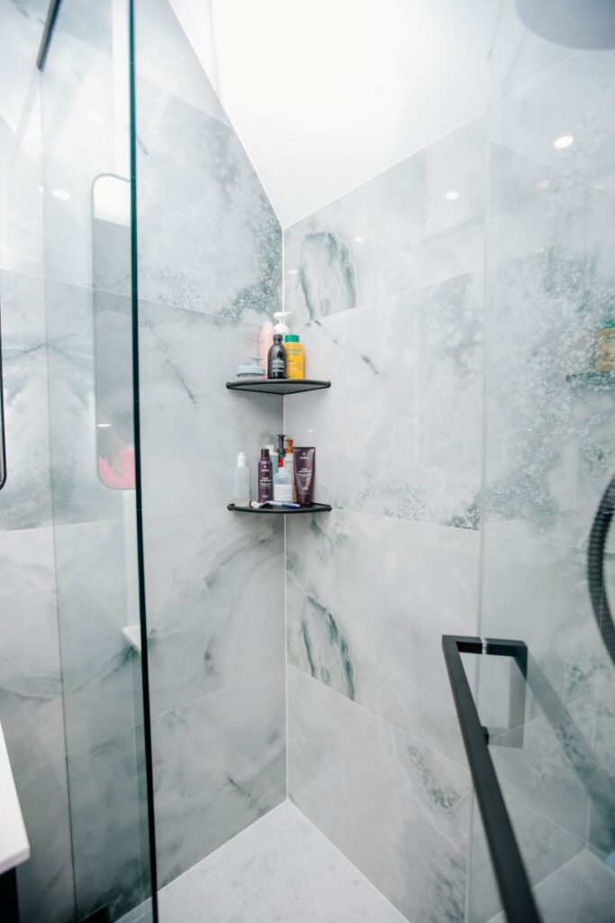 Corner of shower featuring green onyx tiles and two tiered matte black wire corner shelves for storage