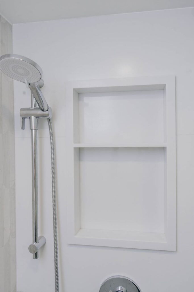 Detail of chrome shower slide bar fixture and a custom built in white tiled niche with dual shelves