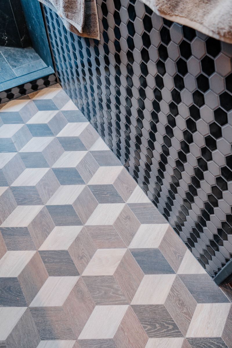 Detail of geometric woodgrain porcelain floor tiles in a 3D cube pattern meeting a black and grey hexagon mosaic wall