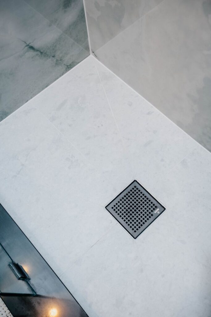 Detail of new white stone look shower floor tile with a modern square drain