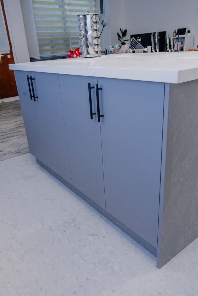 Detail of the custom grey kitchen island with black hardware and a sleek white quartz countertop