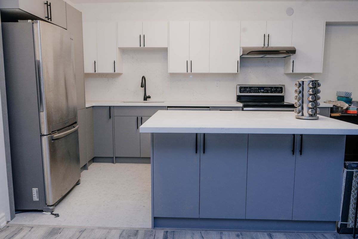 Front view of a condo kitchen remodel with two tone cabinetry, quartz countertops, and a functional island workspace