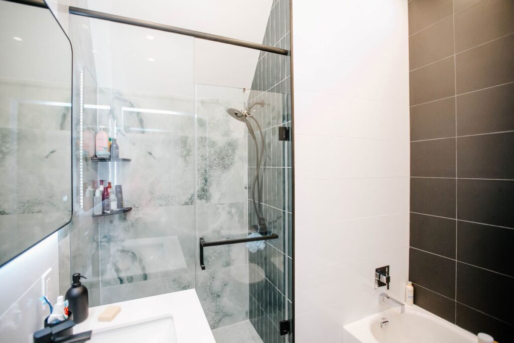 Full view of the renovated shower zone with green tiles and glass door next to the bathtub area