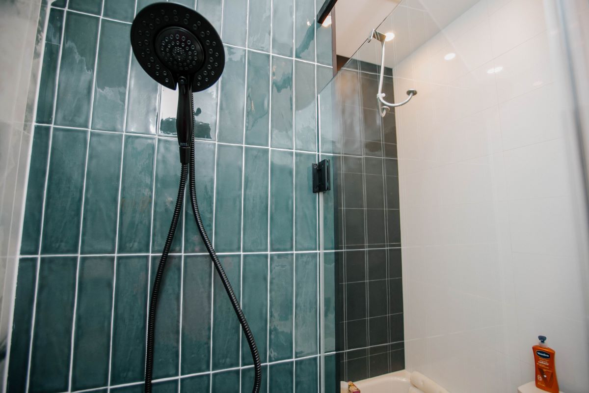 Handheld black shower sprayer on a sliding rail against a green vertical tile wall