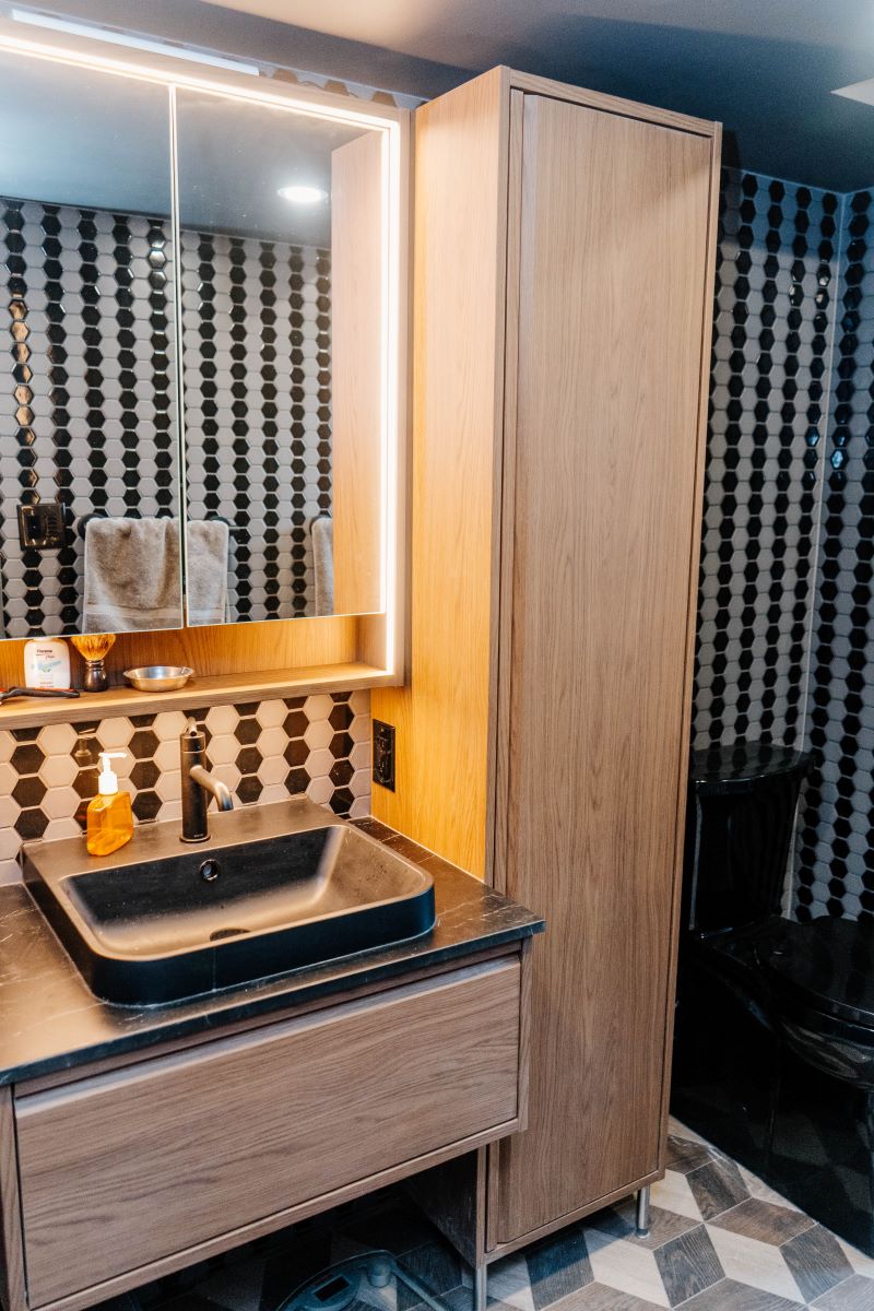 Modern bathroom vanity area with a custom tall wood cabinet, LED backlit mirror, and black vessel sink Vaughan