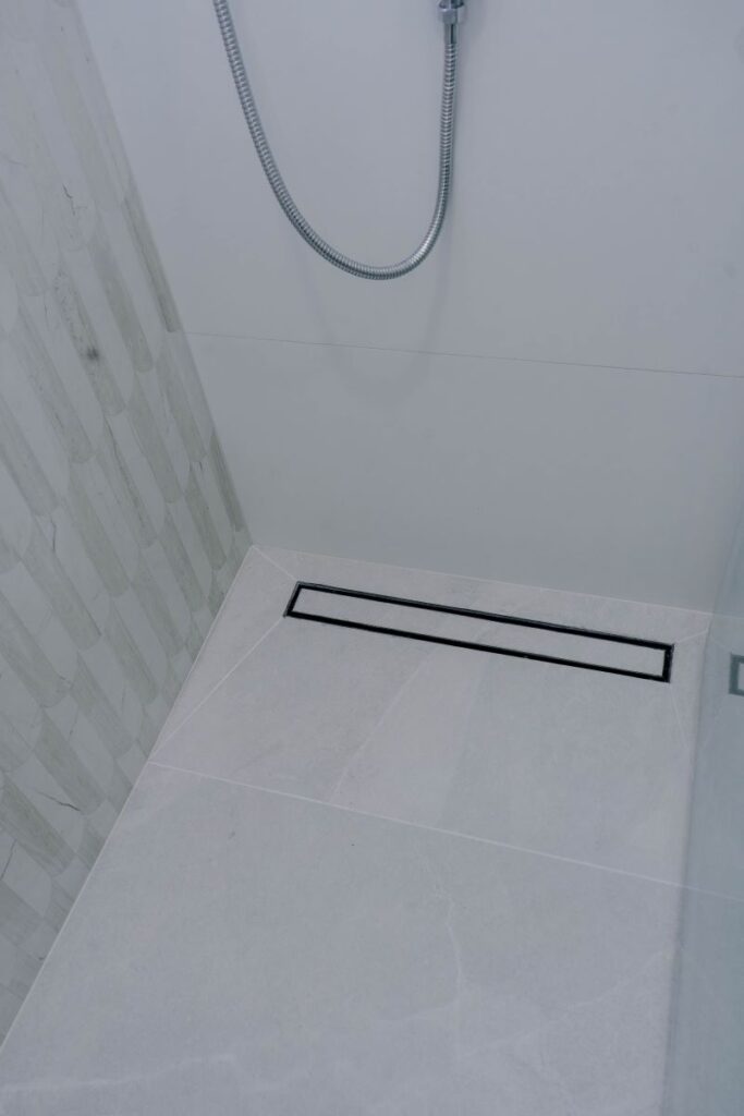 Modern linear shower drain integrated into light grey porcelain floor tiles with white scallop wall tiles
