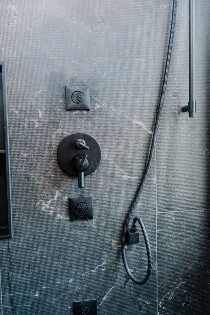 Modern matte black shower valve and body jet controls mounted on textured dark grey porcelain shower walls