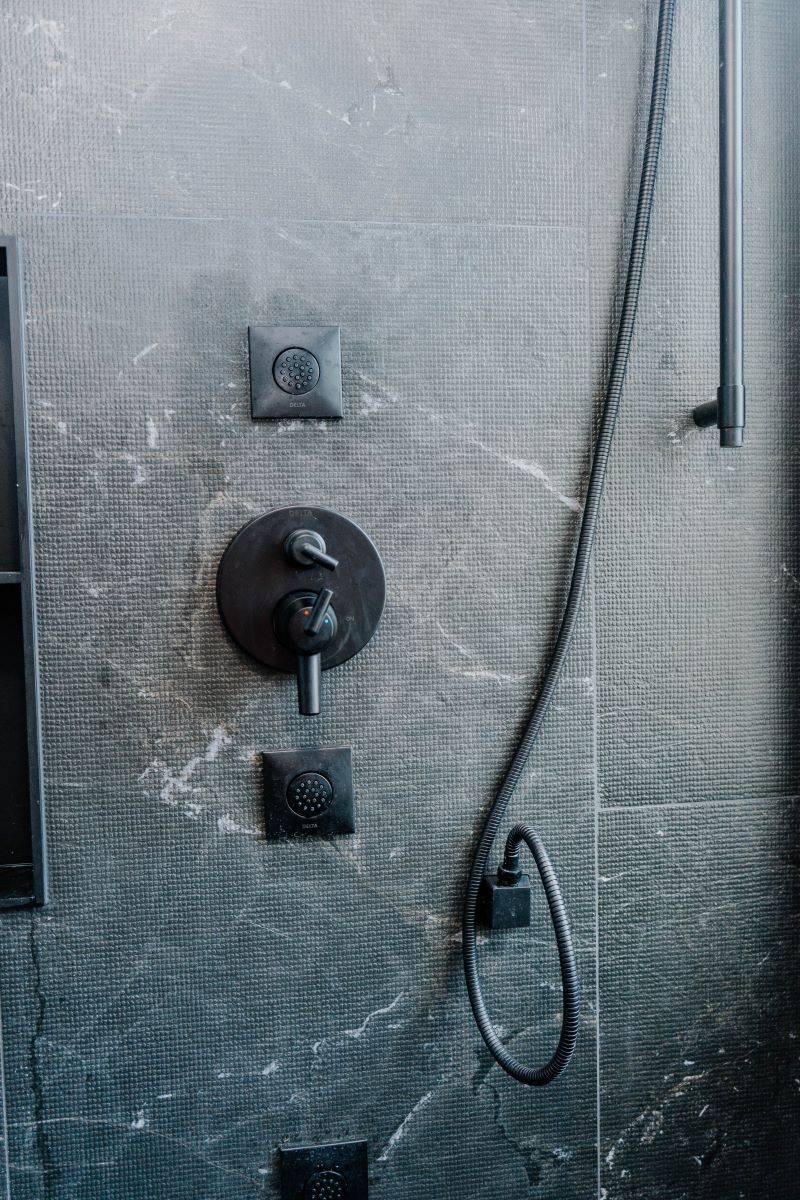 Modern matte black shower valve and body jet controls mounted on textured dark grey porcelain shower walls