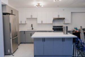 Overview of the kitchen layout with a central island, custom grey cabinetry, white quartz backsplash, and modern lighting