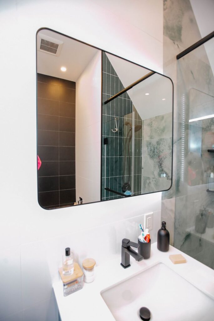 Reflection of green onyx shower tiles in a rectangular black framed mirror above a modern vanity