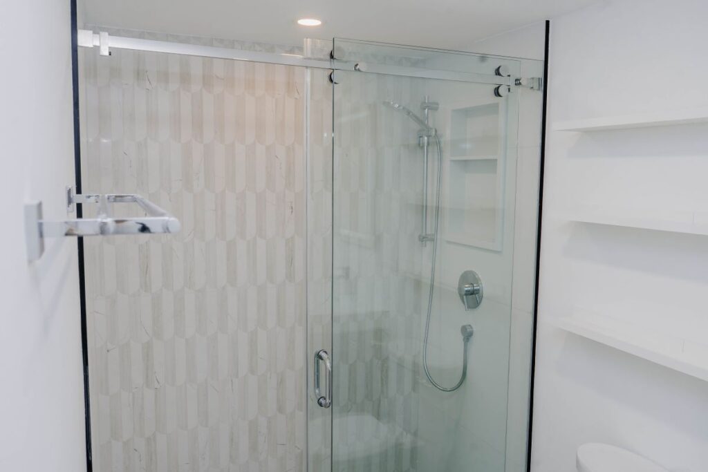 Renovated condo bathroom shower enclosure with sliding glass doors, chrome towel rack, and textured white feature tiles