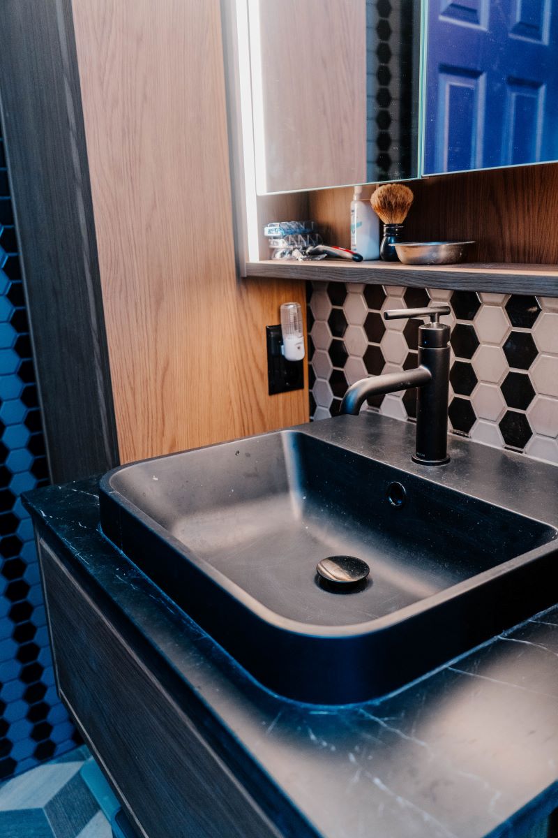 Side view of a matte black vessel sink and faucet installed on a custom wood floating vanity