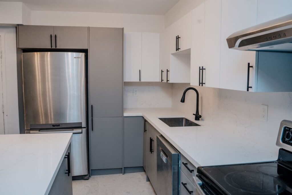 Stainless steel refrigerator integrated into custom full height grey cabinetry in a modern condo kitchen renovation