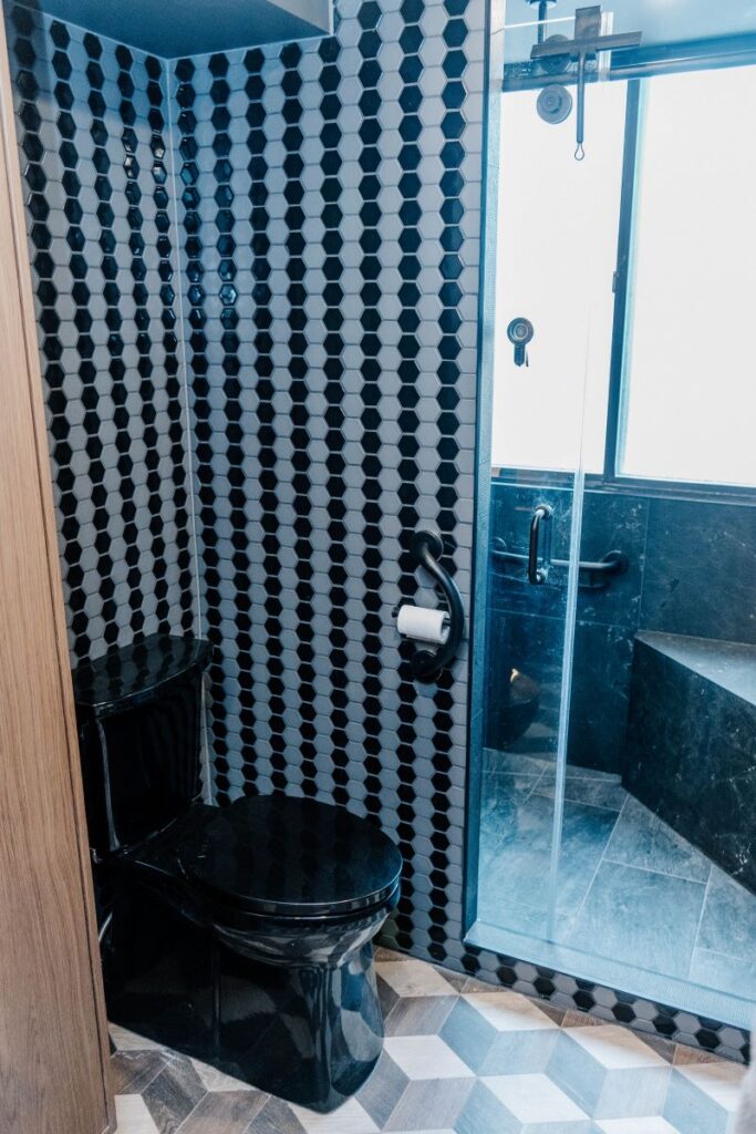 View of the toilet area separated by a custom partition wall, leading into a glass enclosed walk in shower with a bench