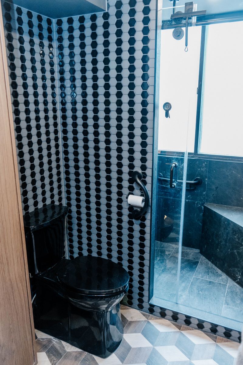 View of the toilet area separated by a custom partition wall, leading into a glass enclosed walk in shower with a bench