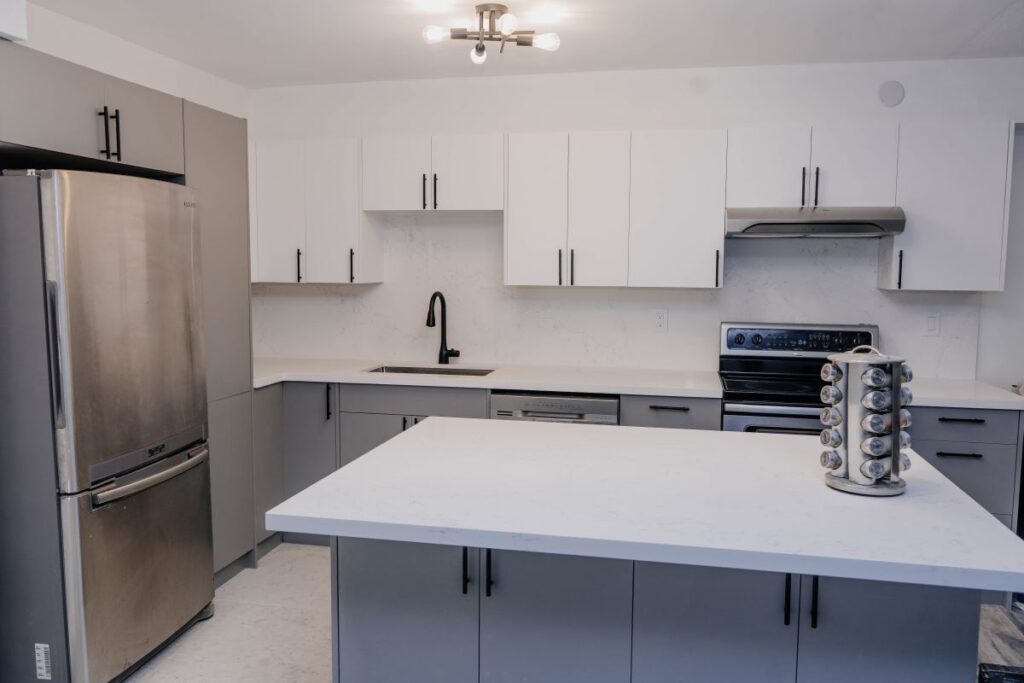 Wide view of a renovated condo kitchen featuring a large grey island with a white quartz countertop and stainless steel appliances