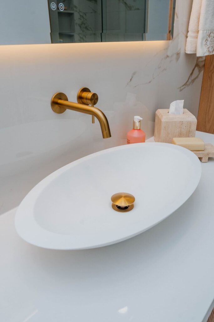 Close up of a brushed gold wall mounted faucet pouring into a white oval vessel sink