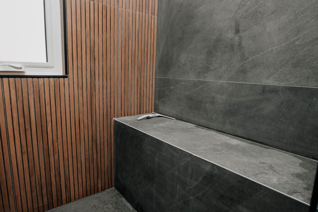 Close up of a dark slate tiled shower bench meeting a wood slat feature wall under a shower window
