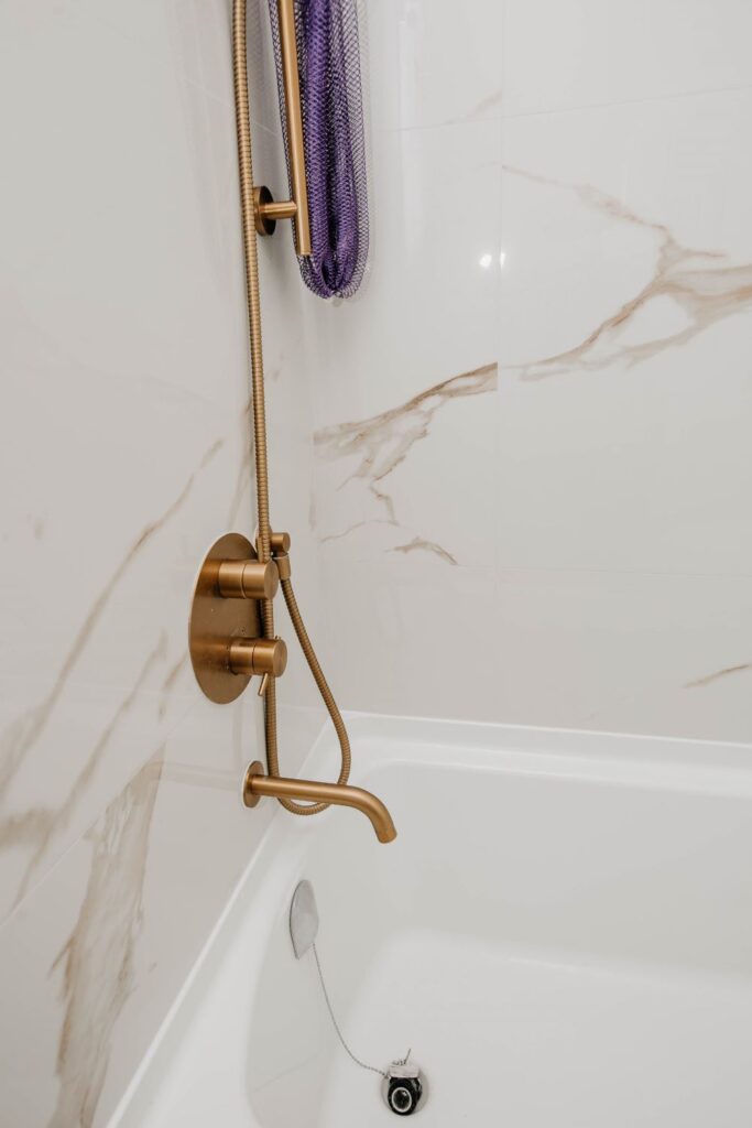 Detail of gold tub spout and diverter valve installation on white marble tile