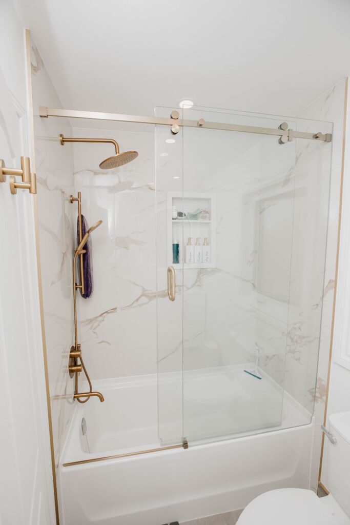 Full view of a tiled tub shower combo with gold hardware and a recessed niche