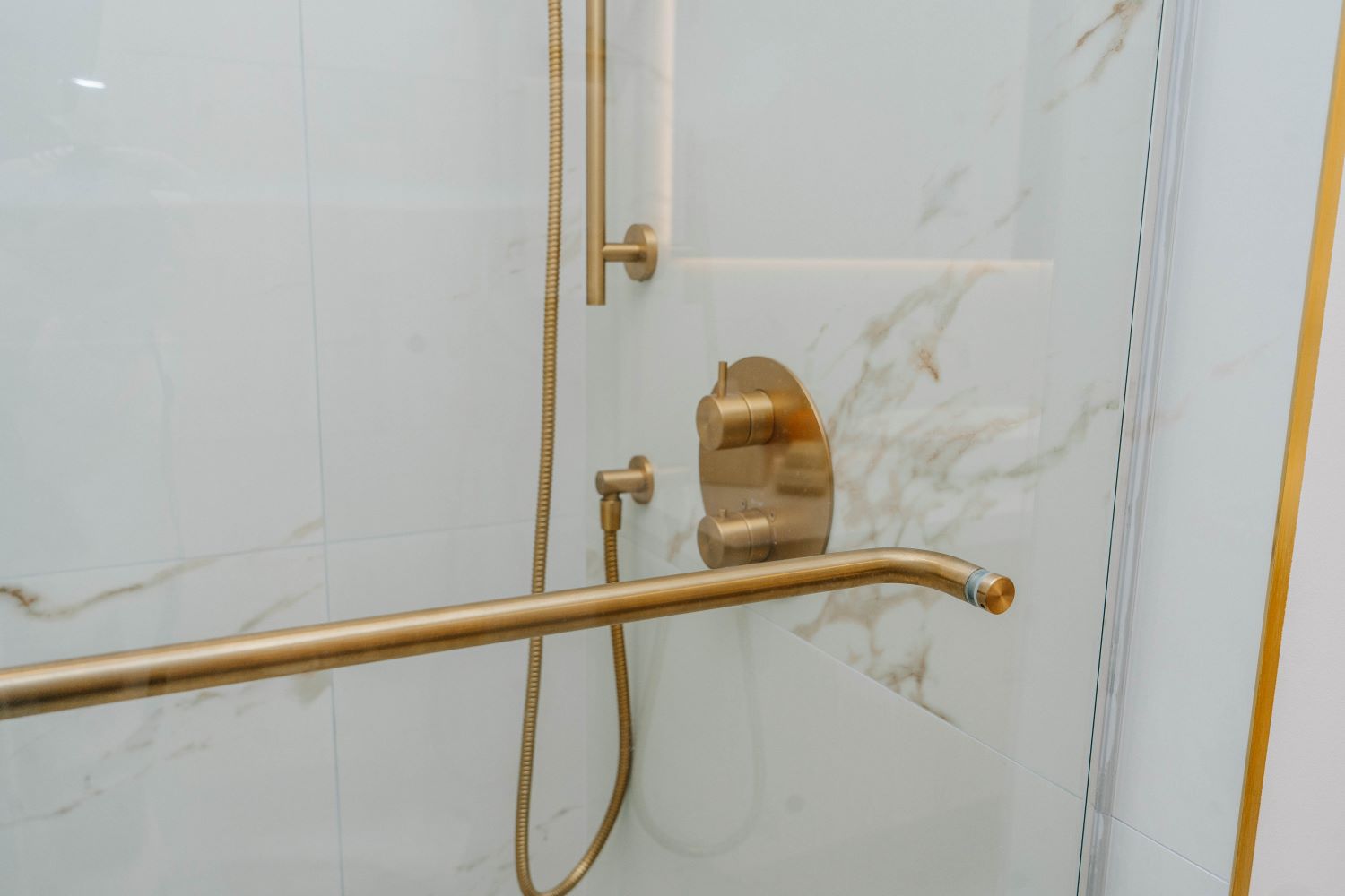 Full view of the gold shower system including slide bar and rain head in a glass enclosed shower