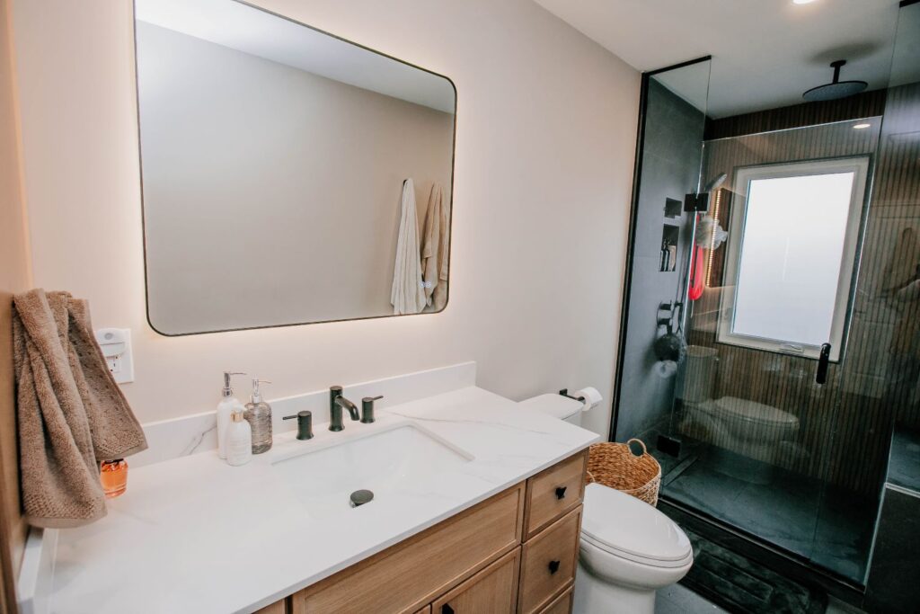 Modern bathroom with light wood vanity, black fixtures, and a dark slate tiled shower