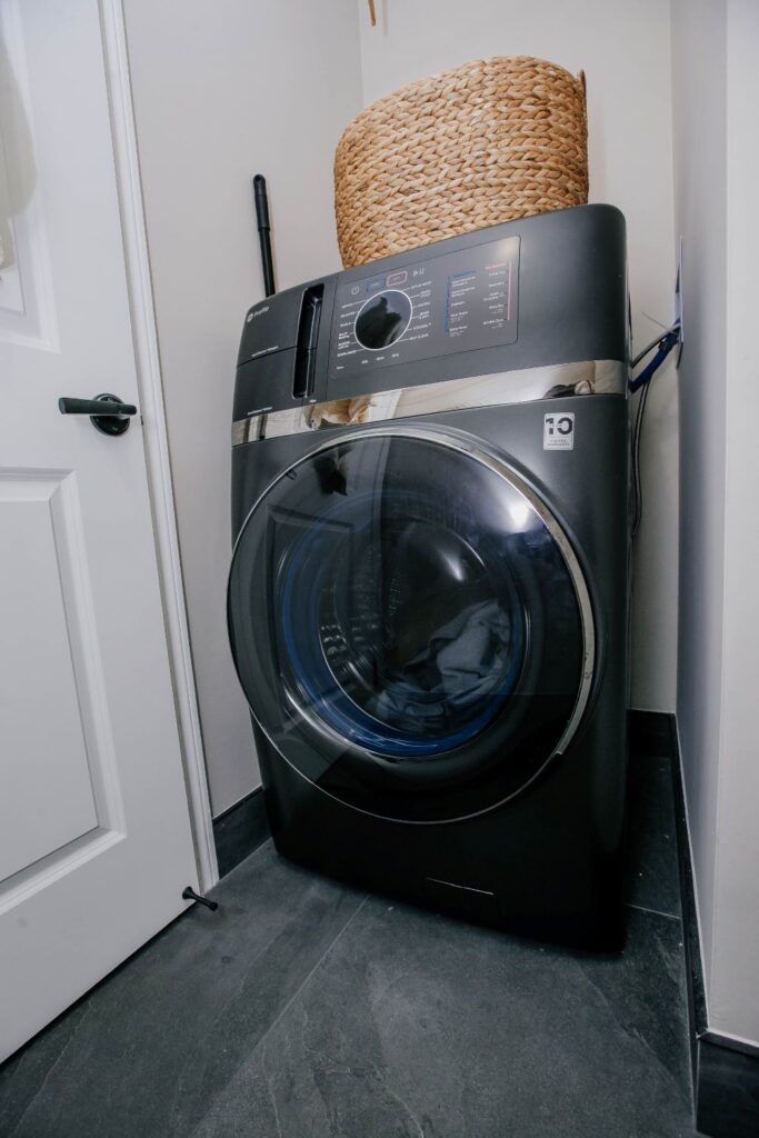 Modern dark grey washing machine installed in a renovated laundry closet with grey tile floor