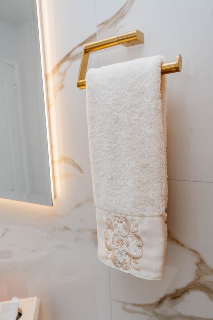 Modern rectangular gold towel ring mounted on a white marble look bathroom wall