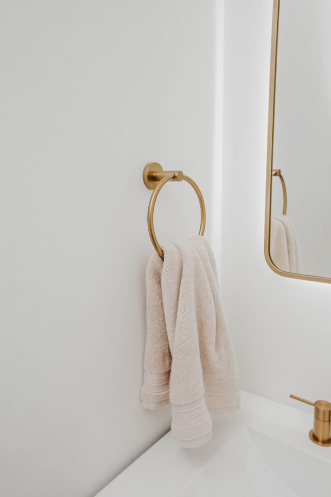 Round gold towel ring and white towel next to an LED mirror