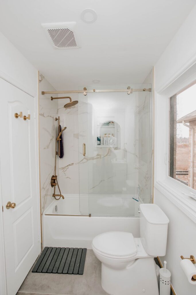 Small bathroom renovation featuring a new toilet, tub with glass doors, and gold accents