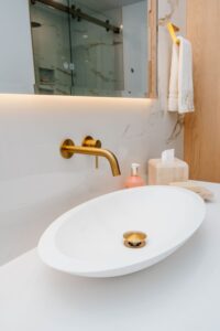 Top down view of a matte white vessel sink with a gold pop up drain and wall mounted faucet