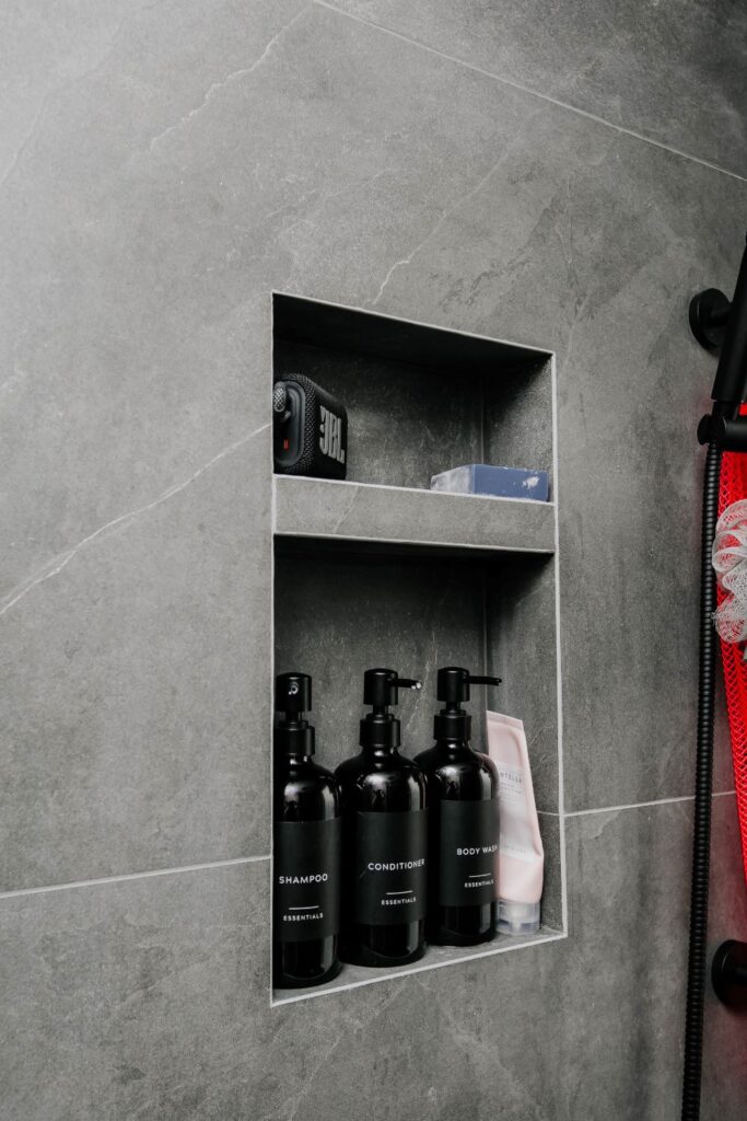 Vertical double shower niche built into dark slate look porcelain tiles, displaying black shampoo bottles