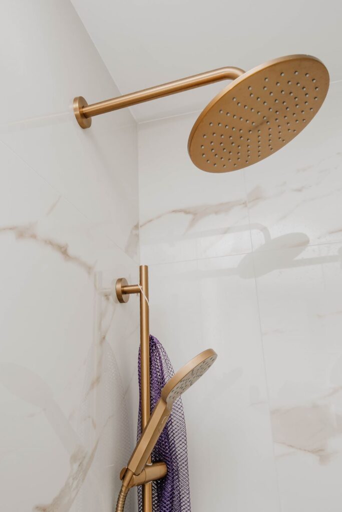 Wall mounted gold rain shower arm installed above a bathtub