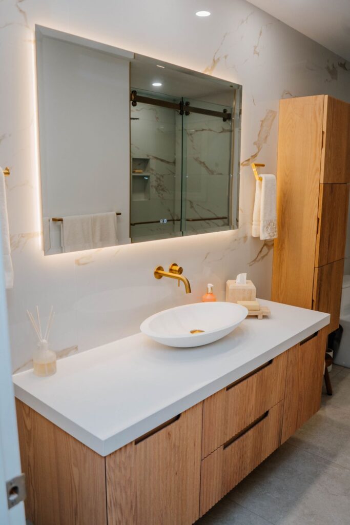 Wide angle view of a luxury Mississauga bathroom with a large LED mirror, fluted oak vanity, and gold wall mounted faucet