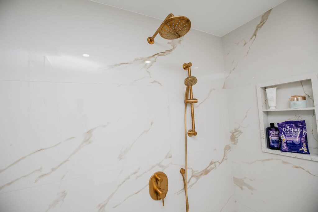 Close up of brushed gold shower fixture set in large format marble look tile shower