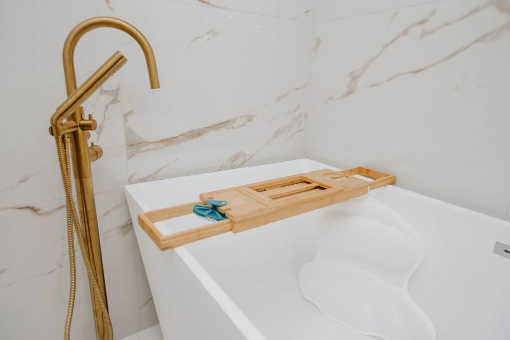 Freestanding bathtub detail with gold tub filler and large format wall tile