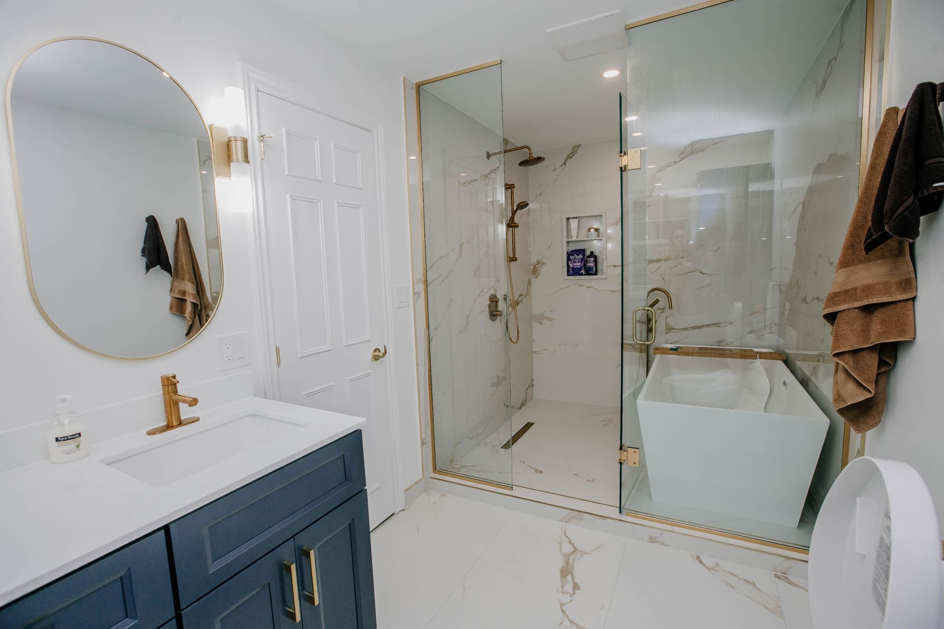 Wide view of renovated master bathroom with navy vanity, glass shower and freestanding tub