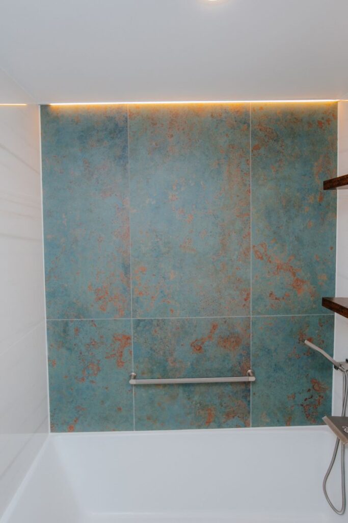 Bathtub feature wall with textured blue green tile and warm LED strip lighting
