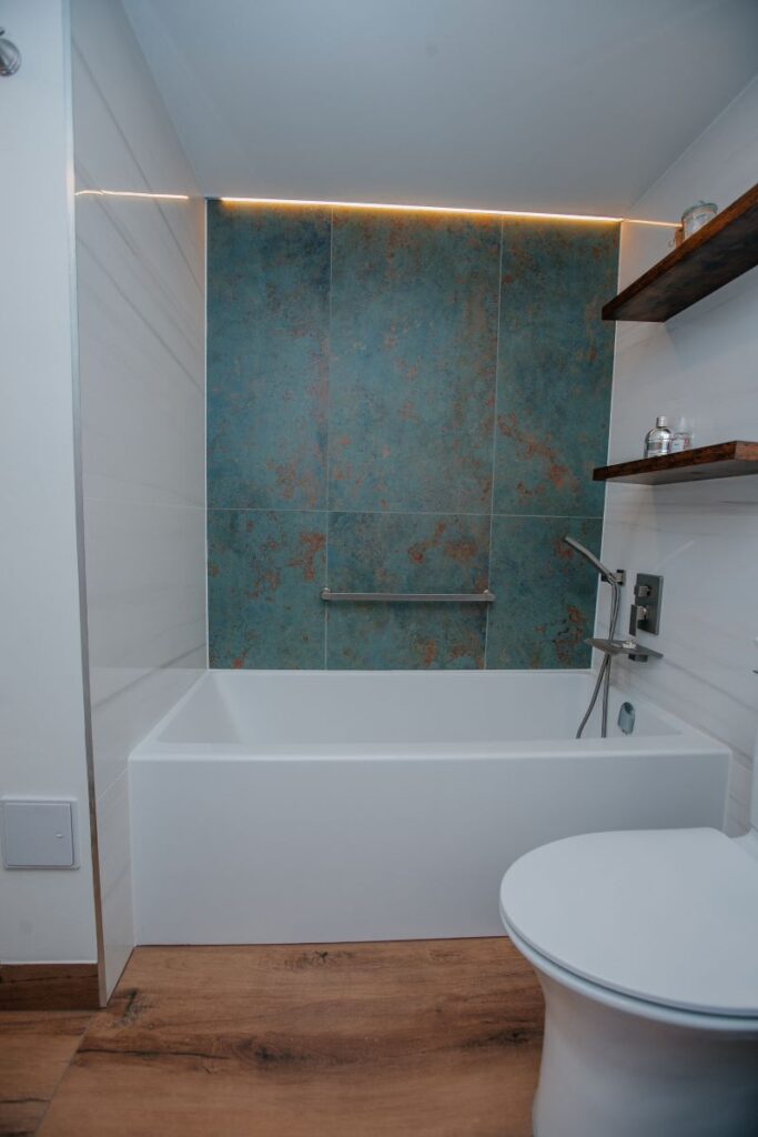 Bathtub wall with blue green feature tile and indirect ceiling lighting