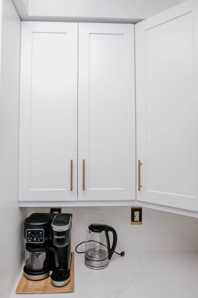 Corner white shaker upper cabinets with brushed gold handles and Keurig coffee station on white quartz countertop