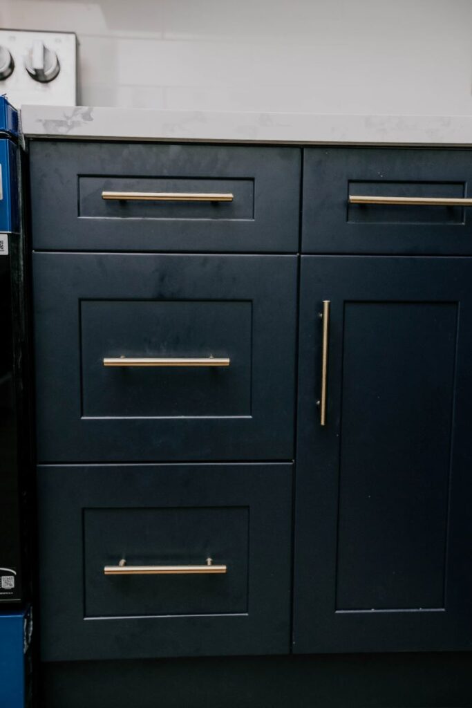 Detail of navy blue shaker lower kitchen cabinets with brushed gold bar handles and white quartz countertop