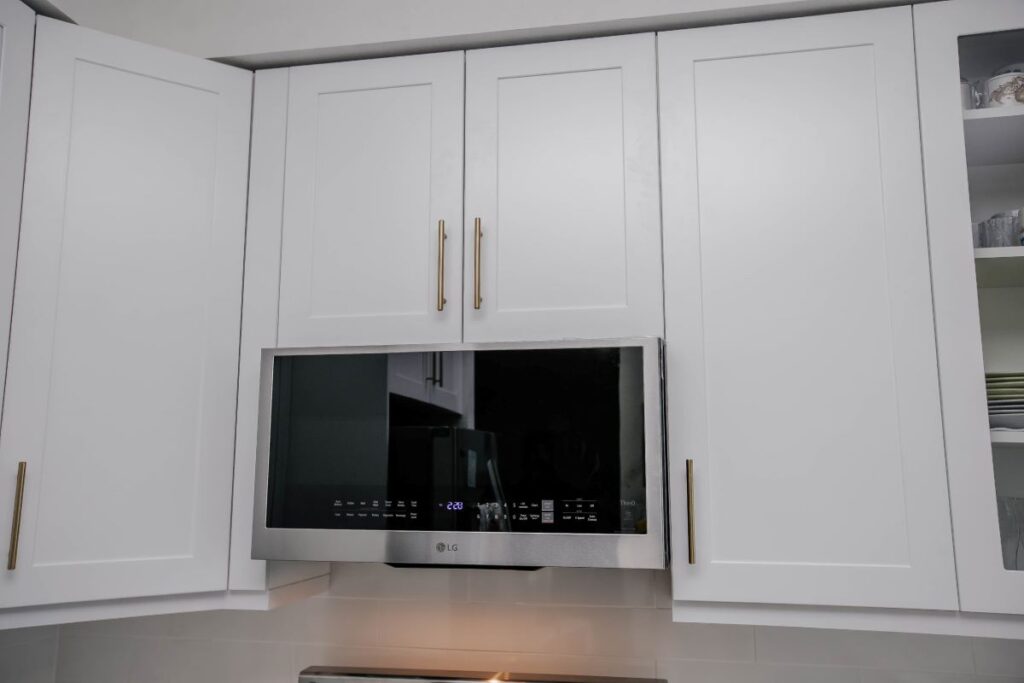 Detail of white shaker upper cabinets with brushed gold bar handles and LG over range stainless microwave