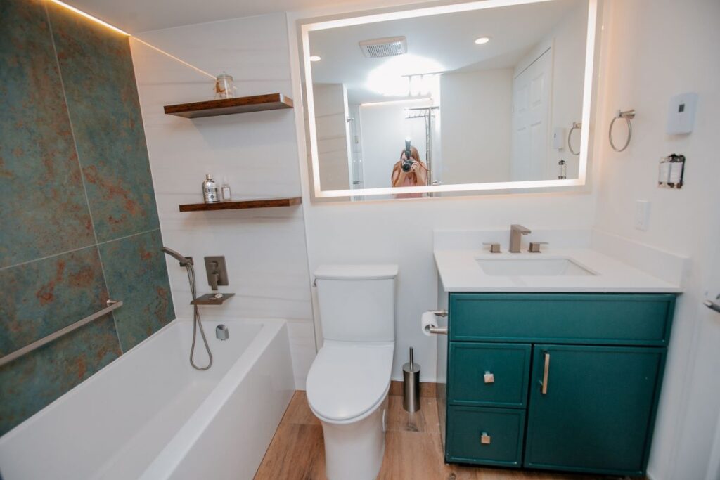 LED mirror, dark green vanity, and bathtub in modern master bathroom