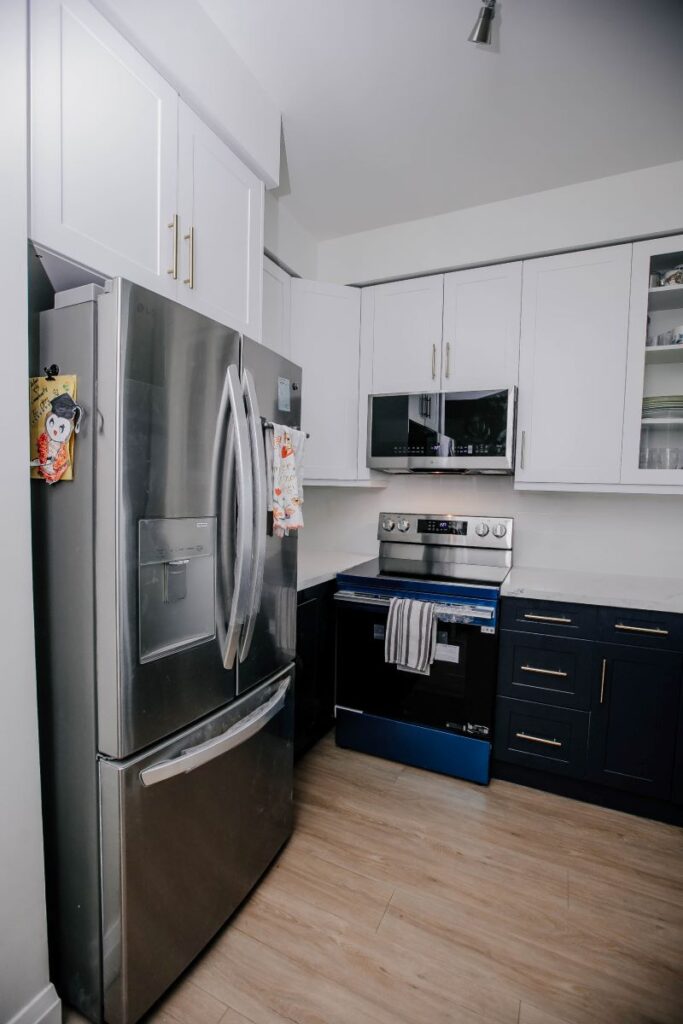 LG stainless steel French door refrigerator beside white shaker upper cabinets with brushed gold handles in renovated condo kitchen